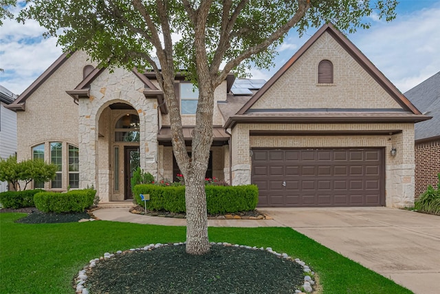 french country home featuring solar panels, brick siding, a front lawn, concrete driveway, and an attached garage
