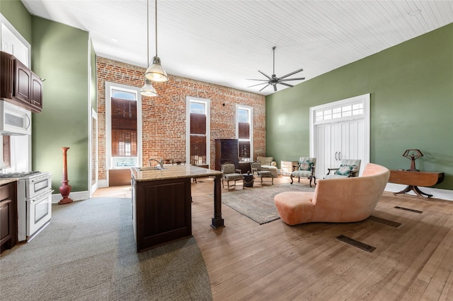 living area with a towering ceiling, wood finished floors, brick wall, and a ceiling fan