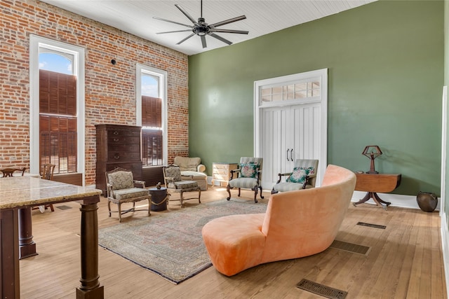sitting room featuring a ceiling fan, visible vents, brick wall, and light wood-type flooring