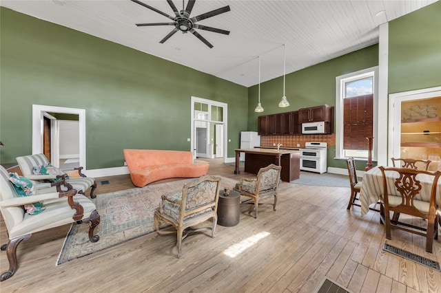living area featuring light wood finished floors, ceiling fan, high vaulted ceiling, and baseboards