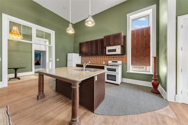 kitchen with white appliances, hanging light fixtures, dark brown cabinets, backsplash, and a sink