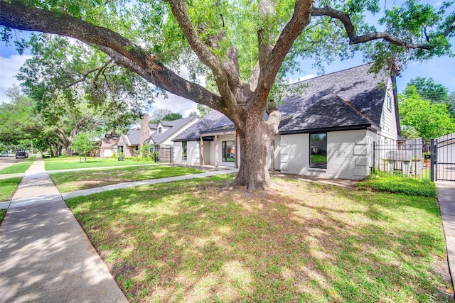 view of front of home featuring a front yard, a shingled roof, a gate, brick siding, and fence