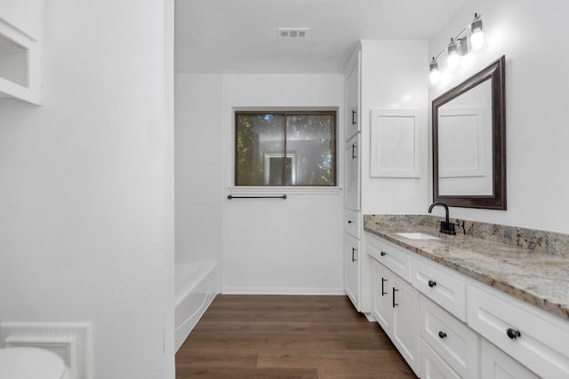 full bath featuring wood finished floors, a bathtub, vanity, baseboards, and visible vents
