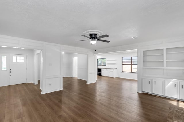 unfurnished living room with a textured ceiling, ceiling fan, dark wood-style floors, and built in shelves