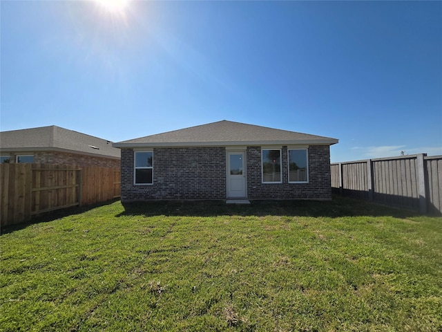 rear view of house featuring brick siding, a fenced backyard, and a lawn