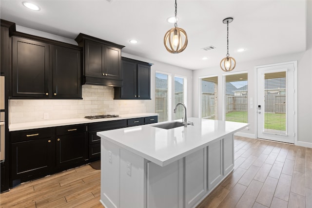 kitchen with light wood finished floors, a sink, decorative backsplash, visible vents, and light countertops