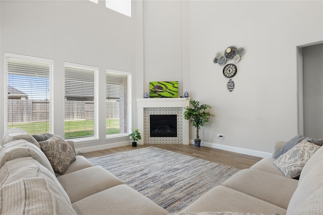 living room featuring baseboards, wood finished floors, a tiled fireplace, and a high ceiling