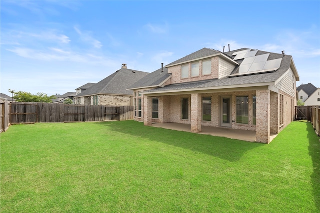 back of property featuring a lawn, a patio, solar panels, and a fenced backyard