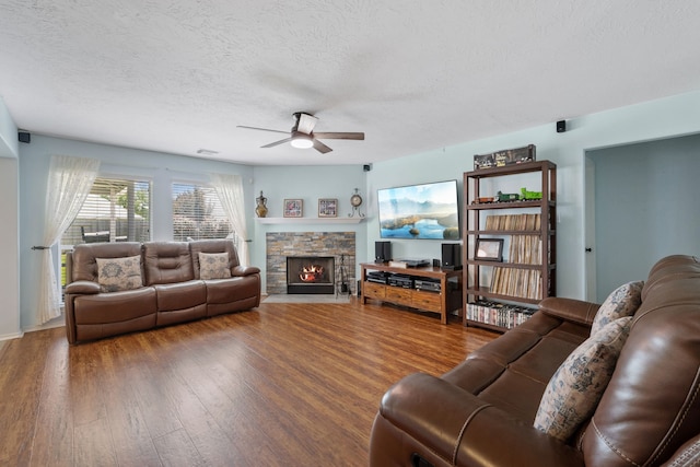 living area with a stone fireplace, a textured ceiling, a ceiling fan, and wood finished floors