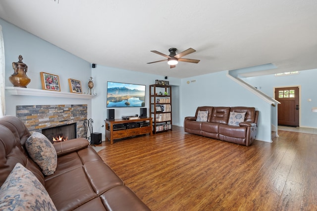 living area featuring stairway, a stone fireplace, a ceiling fan, and wood finished floors