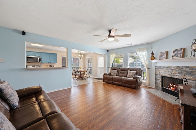 living area featuring ceiling fan with notable chandelier, wood finished floors, a textured ceiling, a fireplace, and baseboards