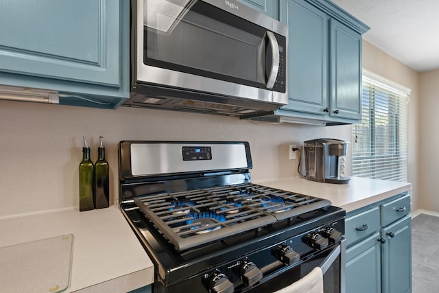 kitchen with baseboards, blue cabinets, light tile patterned flooring, light countertops, and appliances with stainless steel finishes
