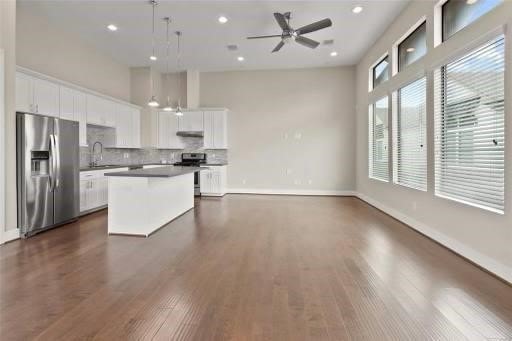 kitchen featuring stainless steel appliances, dark wood-type flooring, a kitchen island, white cabinetry, and open floor plan