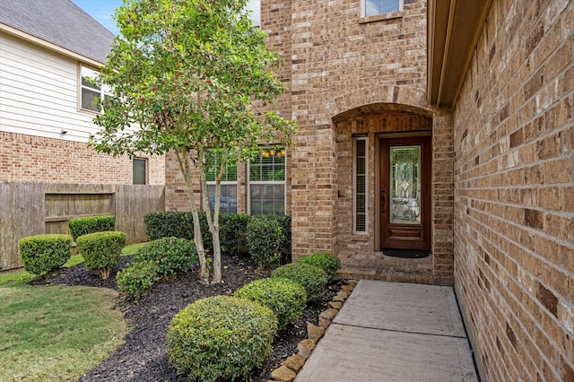 view of exterior entry featuring fence and brick siding