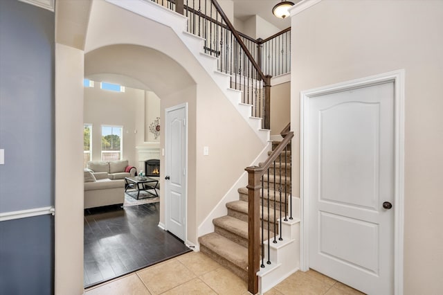 stairway featuring a lit fireplace, a high ceiling, arched walkways, and tile patterned floors