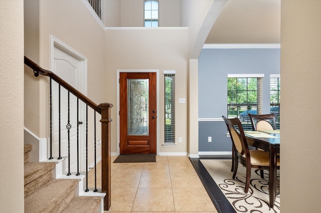tiled entryway featuring baseboards, stairway, a healthy amount of sunlight, and crown molding