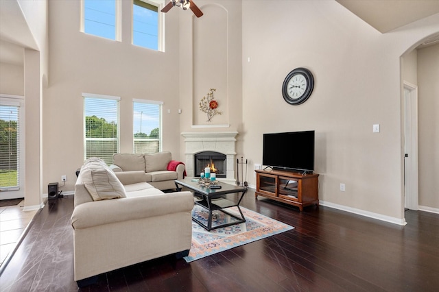 living area featuring baseboards, a ceiling fan, a healthy amount of sunlight, and a towering ceiling