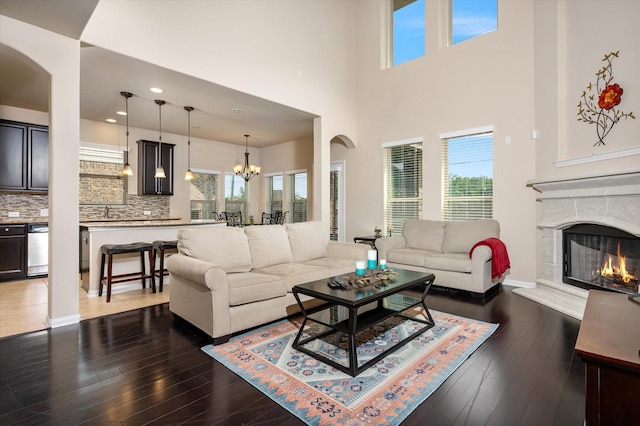 living room featuring a high ceiling, a chandelier, baseboards, a high end fireplace, and wood finished floors
