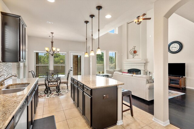 kitchen with a sink, a warm lit fireplace, a center island, decorative light fixtures, and ceiling fan with notable chandelier
