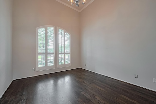 spare room with an inviting chandelier, crown molding, dark wood-style floors, and baseboards