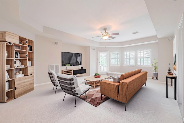 living area with light colored carpet, ceiling fan, a raised ceiling, visible vents, and baseboards