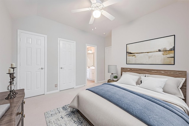 bedroom with lofted ceiling, connected bathroom, light colored carpet, baseboards, and a ceiling fan