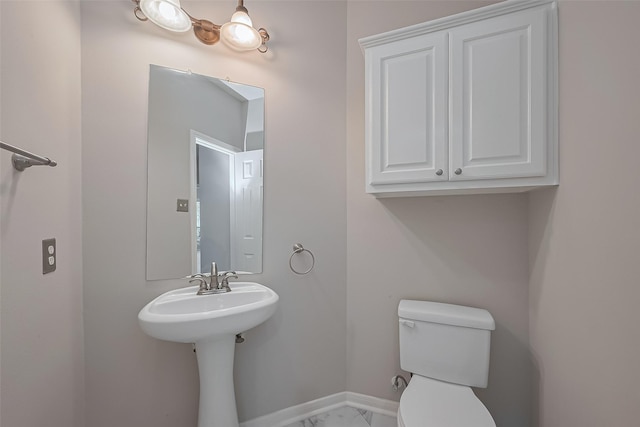 half bath with a sink, toilet, marble finish floor, and baseboards