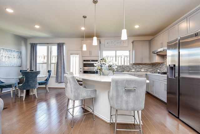 kitchen featuring gray cabinetry, plenty of natural light, stainless steel appliances, and under cabinet range hood