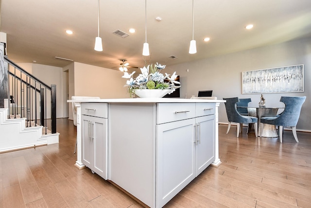 kitchen featuring visible vents, ceiling fan, a kitchen island, light countertops, and light wood finished floors