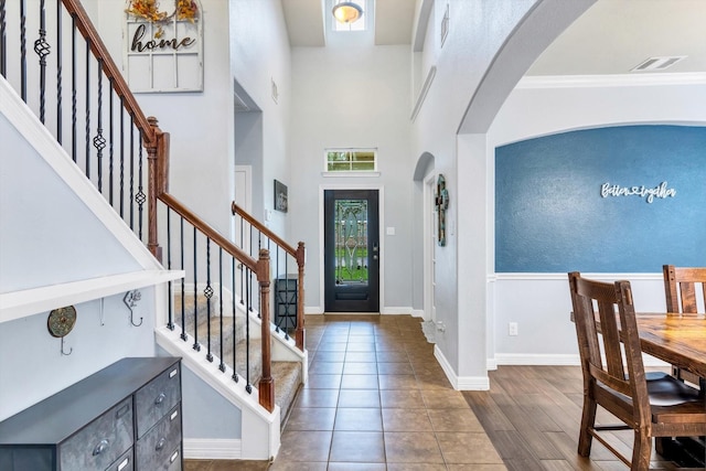 foyer entrance with crown molding, stairway, visible vents, baseboards, and arched walkways