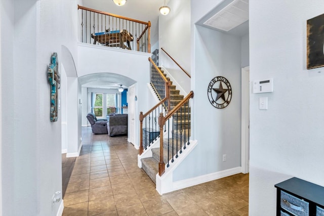 stairway with arched walkways, tile patterned floors, ceiling fan, baseboards, and visible vents