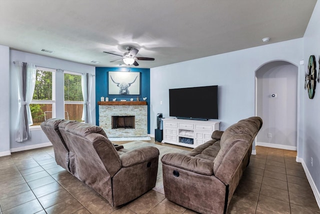 tiled living room with visible vents, baseboards, arched walkways, a fireplace, and a ceiling fan