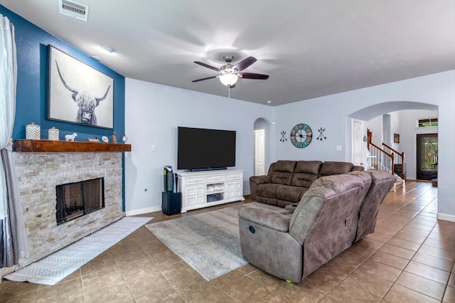 tiled living room featuring visible vents, arched walkways, ceiling fan, and a stone fireplace