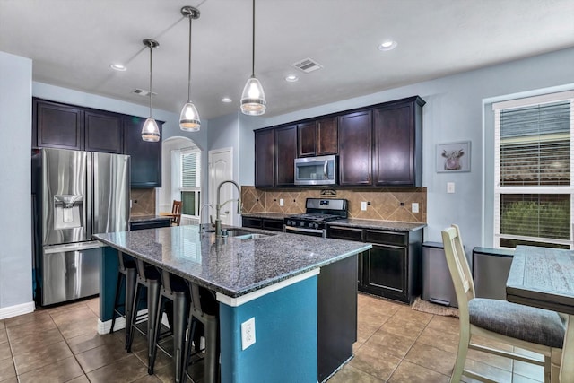 kitchen with dark stone countertops, appliances with stainless steel finishes, dark brown cabinets, a sink, and visible vents