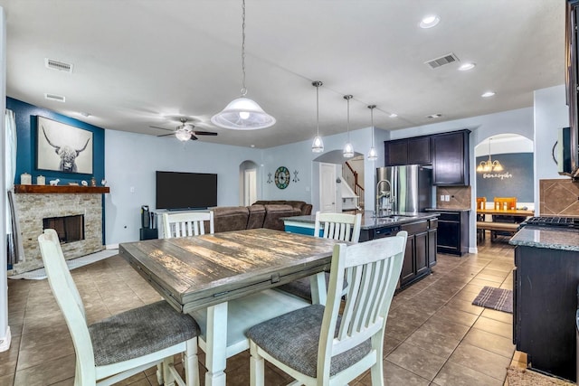 tiled dining area featuring visible vents, arched walkways, a ceiling fan, and a fireplace