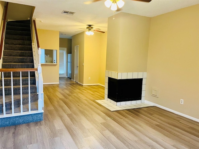 unfurnished living room featuring a ceiling fan, visible vents, a tiled fireplace, and wood finished floors