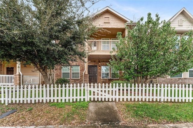 view of property hidden behind natural elements featuring brick siding, a balcony, and a fenced front yard