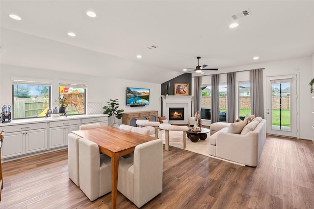 dining room with a warm lit fireplace, ceiling fan, a wealth of natural light, and lofted ceiling