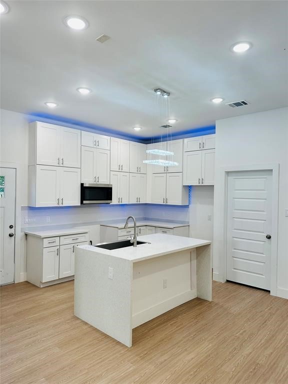 kitchen with visible vents, a sink, light wood-style floors, and stainless steel microwave