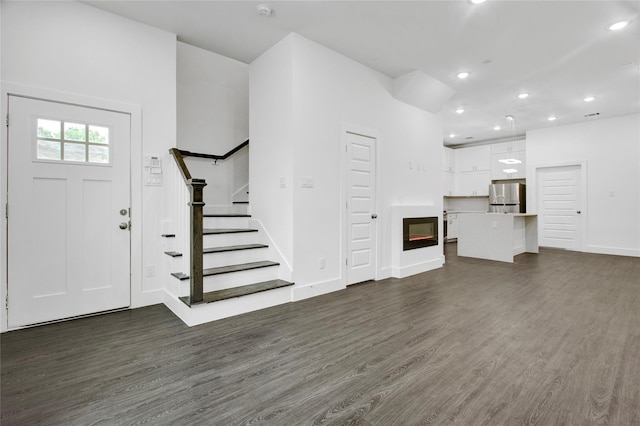 unfurnished living room featuring dark wood finished floors, a glass covered fireplace, stairs, recessed lighting, and baseboards