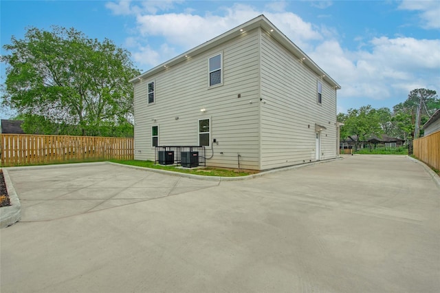 rear view of property featuring central air condition unit, fence, concrete driveway, and a patio area
