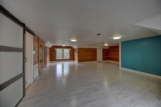 266 Monroe St, Giddings, TX 78942 - empty room featuring wooden walls, light wood-style floors, baseboards, and a barn door
