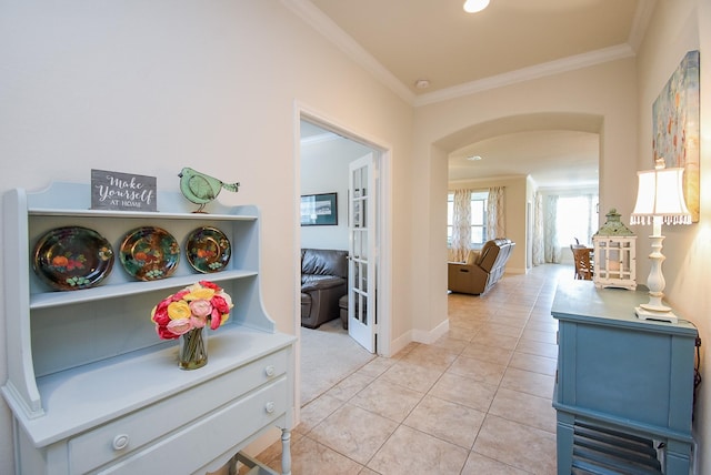 corridor featuring arched walkways, ornamental molding, light tile patterned floors, and baseboards