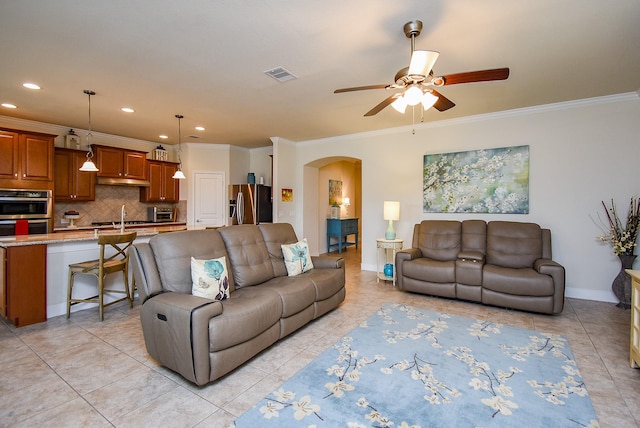 living room with crown molding, arched walkways, a ceiling fan, and visible vents