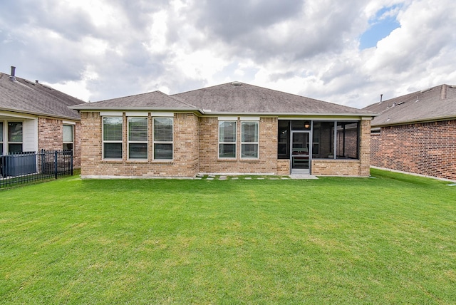 rear view of property with brick siding, a sunroom, fence, and a lawn