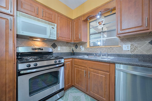 kitchen with dark countertops, stainless steel appliances, decorative backsplash, and a sink
