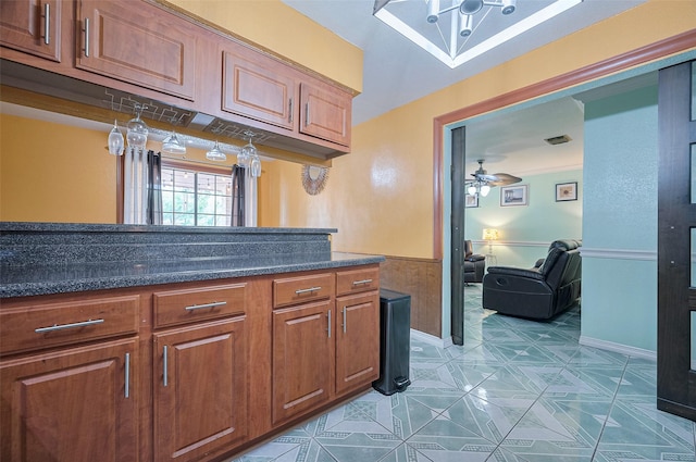 kitchen with ceiling fan, a wainscoted wall, brown cabinetry, and baseboards