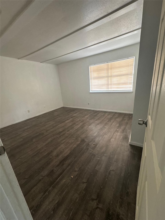 spare room with beam ceiling, baseboards, and dark wood-type flooring