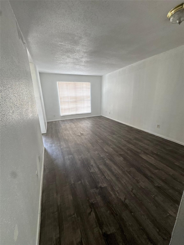 empty room featuring a textured ceiling, baseboards, and dark wood-type flooring