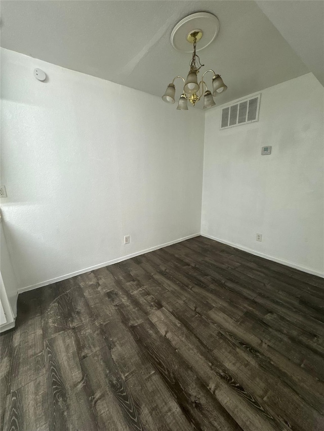 unfurnished dining area featuring dark wood-style floors, an inviting chandelier, visible vents, and baseboards